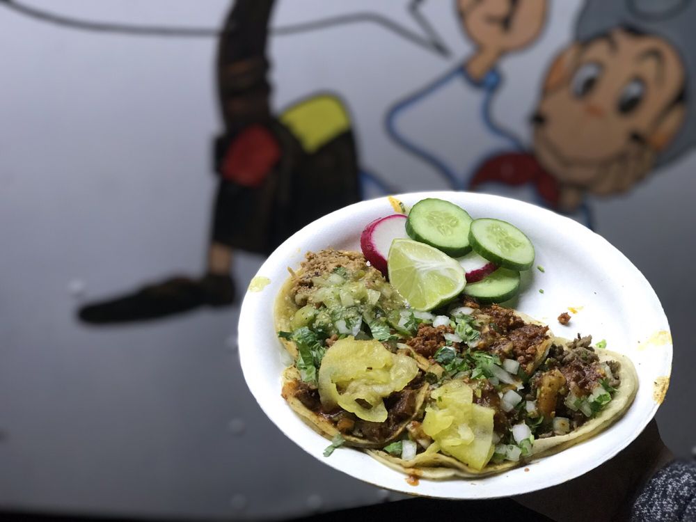 Plate of tacos with cucumber and lime in front of the truck's cartoon mural