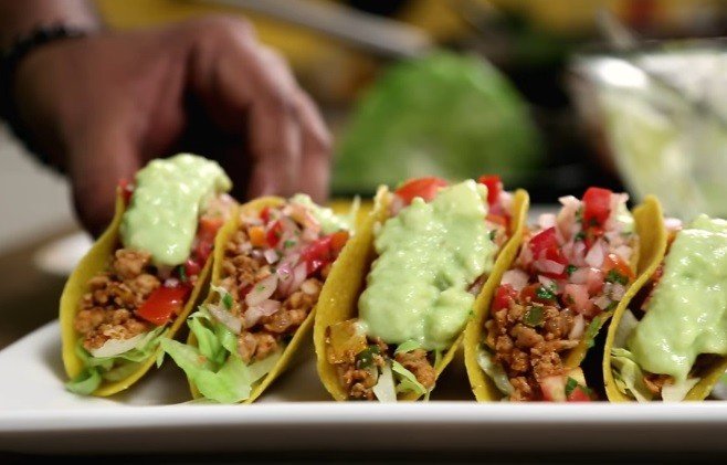 Row of tacos topped with guacamole and pico de gallo