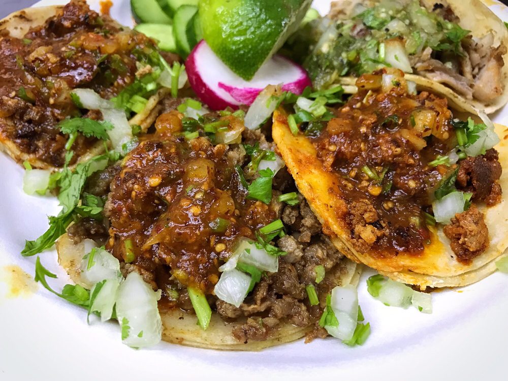 Tacos topped with red salsa, onion, cilantro, radish and lime